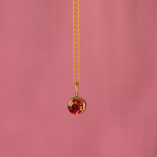 Gold necklace with a red gemstone pendant on a pink background