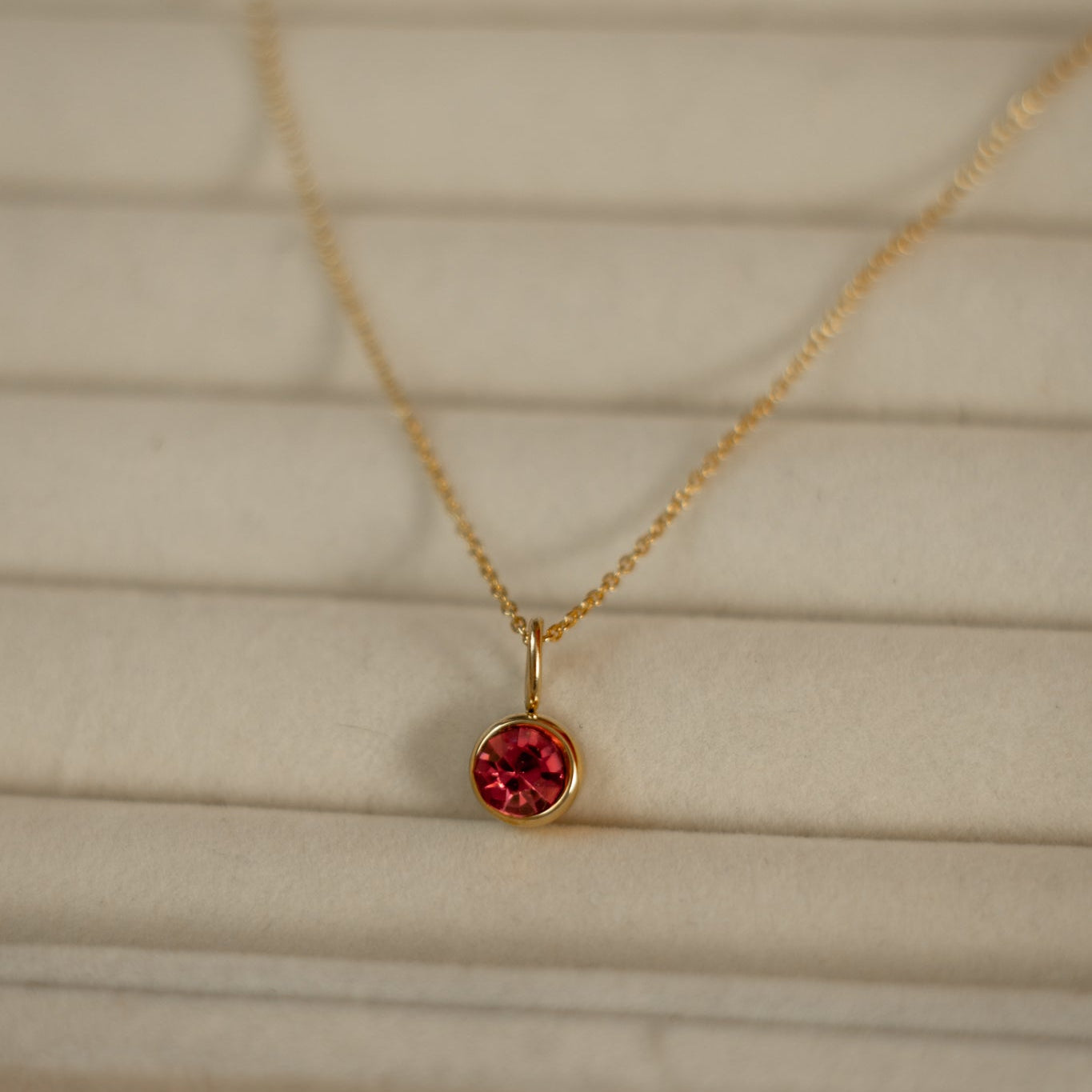 Gold necklace with a red gemstone pendant on a beige background