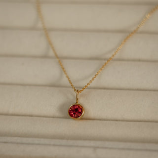 Gold necklace with a red gemstone pendant on a beige background
