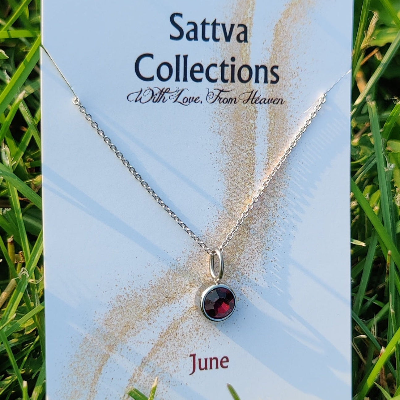 Necklace with a red stone on a 'Sattva Collections' card in grass