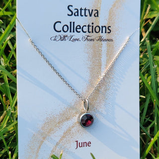 Necklace with a red stone on a 'Sattva Collections' card in grass