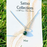 Necklace with a green gemstone on a 'Sattva Collections' card in grass