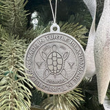 A pewter ornament with a 'Made in Turtle Island' emblem and a turtle shell design, hanging on a Christmas tree.