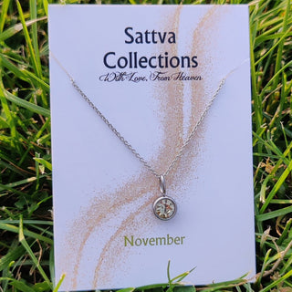 Necklace on a 'Sattva Collections' card with 'November' text, placed on grass.