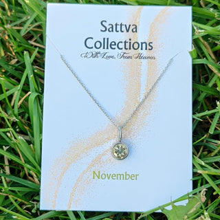 Necklace on a 'Sattva Collections' card with 'November' text, placed on grass.