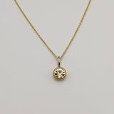 Gold necklace with a round pendant on a light gray background