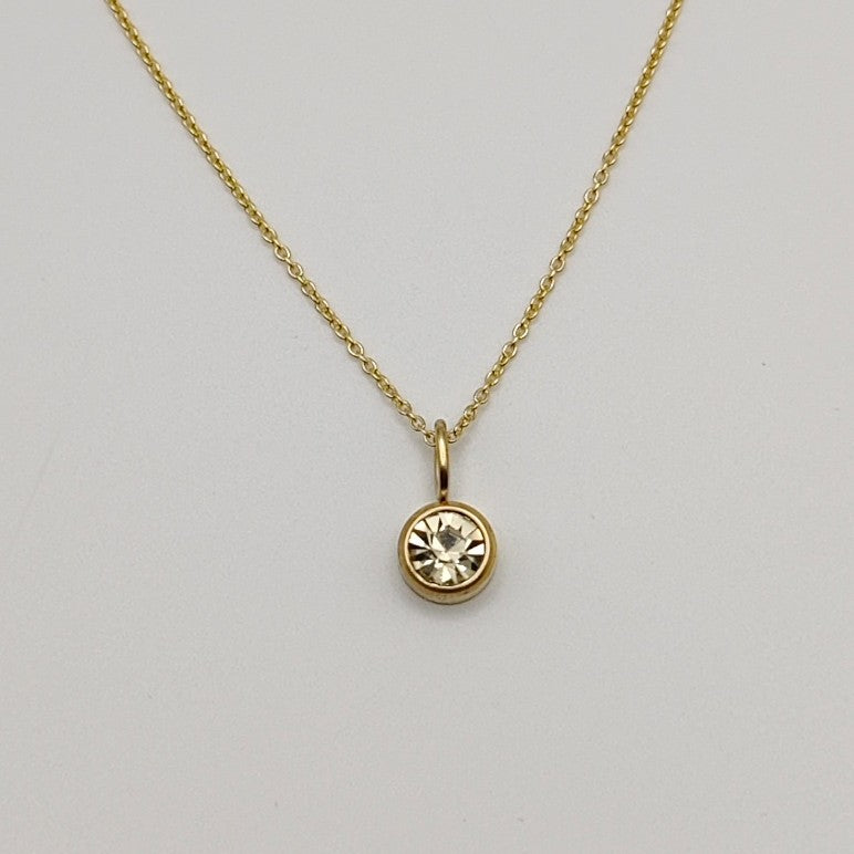 Gold necklace with a round pendant on a light gray background