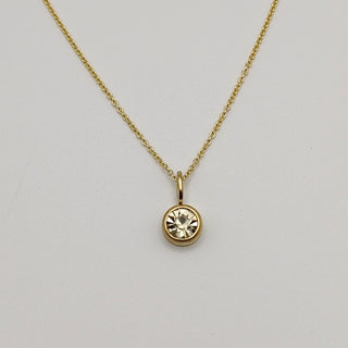 Gold necklace with a round pendant on a light gray background