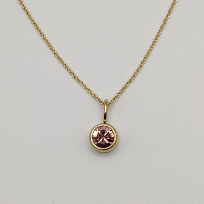 Gold necklace with a pink gemstone pendant on a light gray background