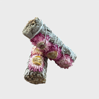 Two rolled white sage smudge sticks with pink sunflowers on a light gray background
