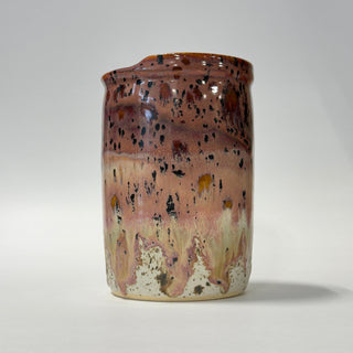 A handmade ceramic jar with a rustic, dripping glaze finish. The glaze transitions from a warm reddish-brown at the top to a dusty pink and cream at the bottom, heavily speckled with dark brown and black mineral flecks.