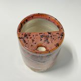 A handmade ceramic planter with a plum and orange glaze, black speckles, and a small central hole, shown from a top-down angle on a white background.