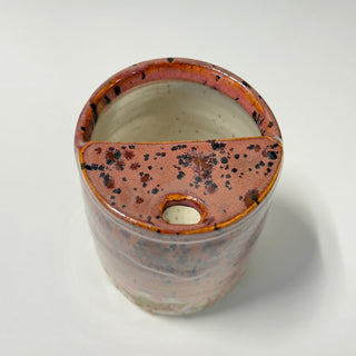 A handmade ceramic planter with a plum and orange glaze, black speckles, and a small central hole, shown from a top-down angle on a white background.