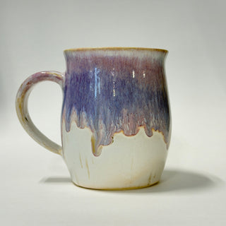 A handmade ceramic mug with a dripping glaze design, featuring a white base, a purple and blue middle section, and a brown rim, set against a plain light gray background.