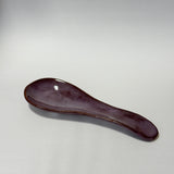A small ceramic spoon rest with a glossy dark purple glaze, photographed on a neutral light gray background.