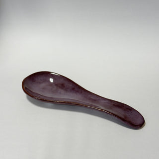 A small ceramic spoon rest with a glossy dark purple glaze, photographed on a neutral light gray background.