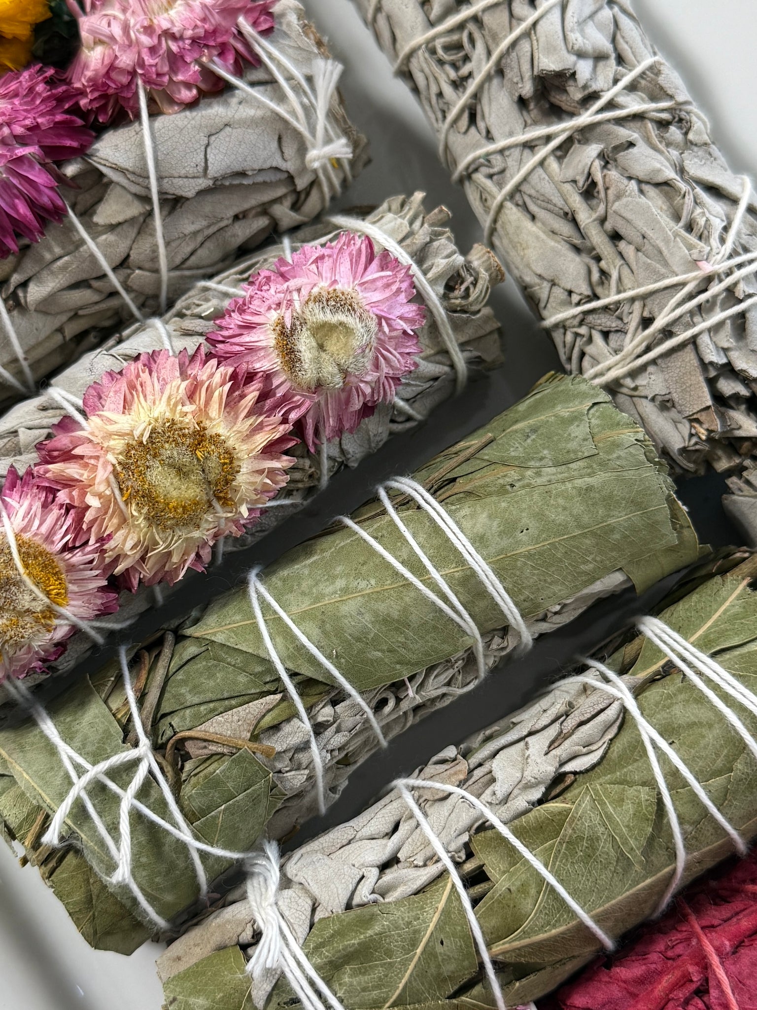 Rolled sage smudge sticks with flowers and twine on a white background