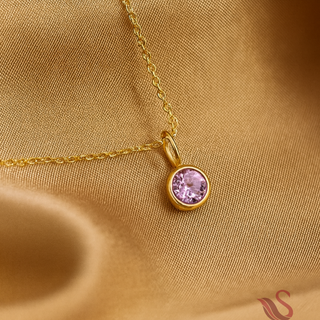 Gold necklace with a pink gemstone pendant on a gold fabric background