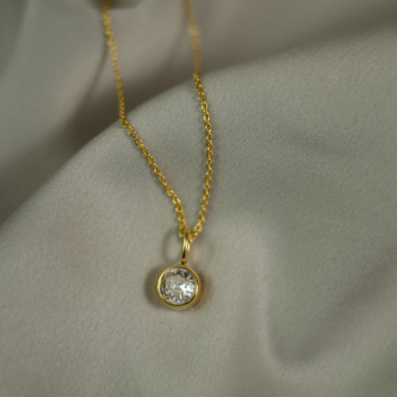 Gold necklace with a diamond pendant on a light fabric background