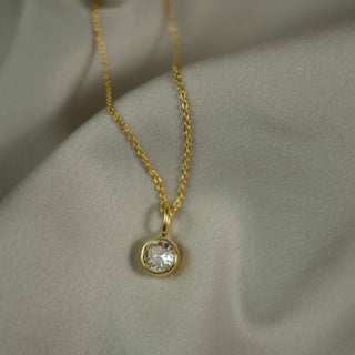 Gold necklace with a diamond pendant on a light fabric background