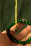 Green beaded bracelet with a gold chain held in a hand against a blurred green background