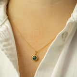 Gold necklace with a green gemstone pendant worn by a person in a white shirt.