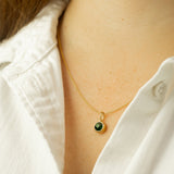 Gold necklace with a green gemstone pendant worn by a person in a white shirt.