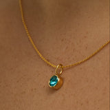 Gold necklace with a blue gemstone pendant on a person's neck
