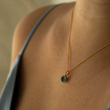 Necklace with a green gemstone pendant on a person wearing a gray top.