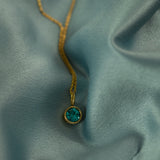Necklace with a green gemstone pendant on a textured blue fabric background