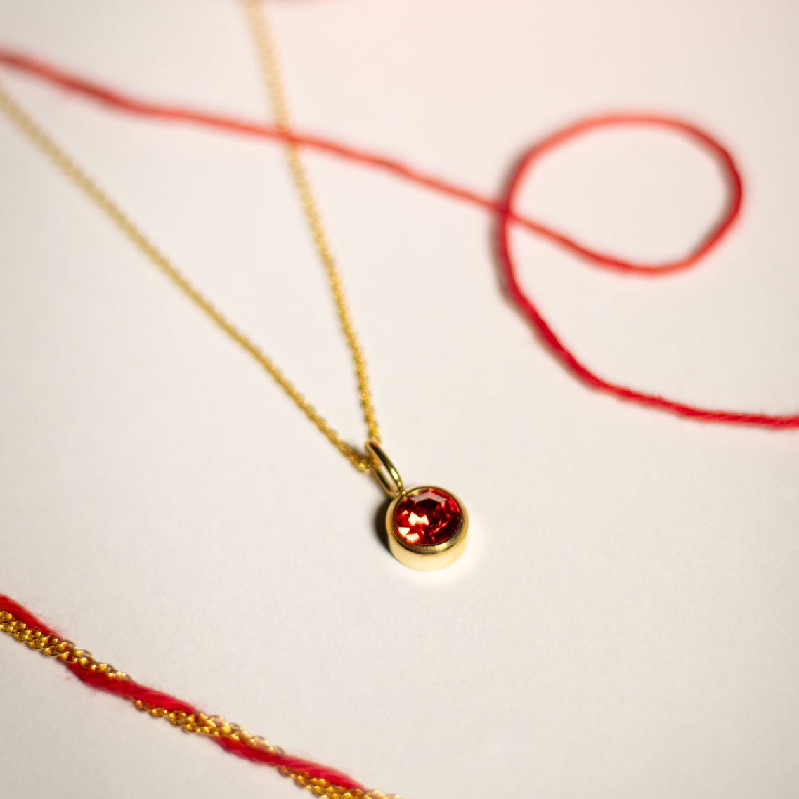 Gold necklace with a red pendant on a white background