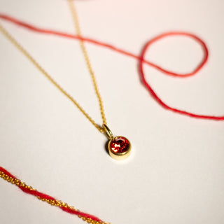 Gold necklace with a red pendant on a white background