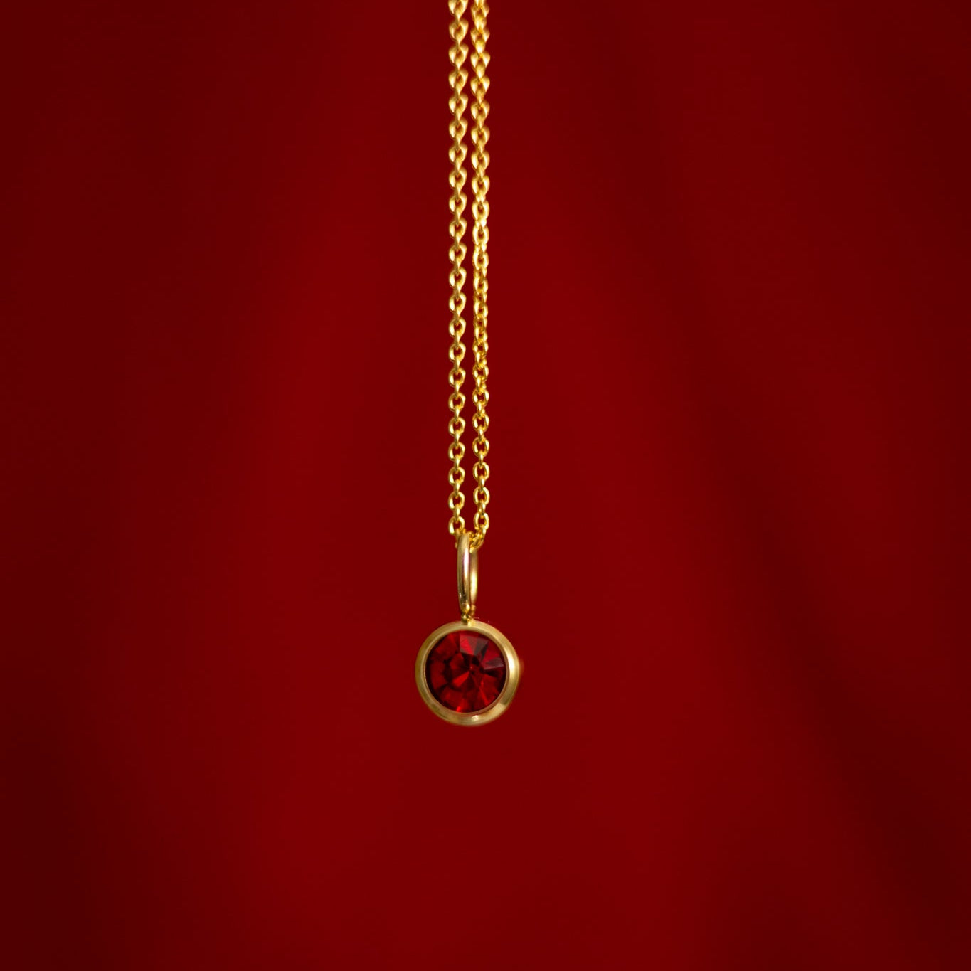 Gold necklace with a red gemstone pendant on a red background