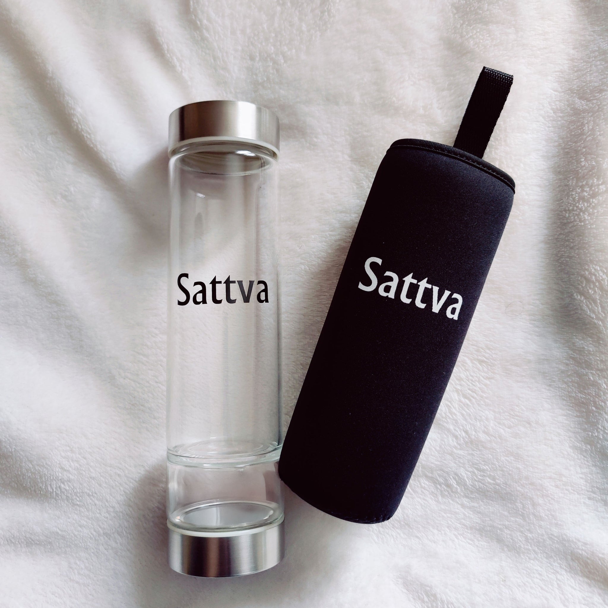 Clear water bottle and black sleeve with 'Sattva' branding on a white fabric background