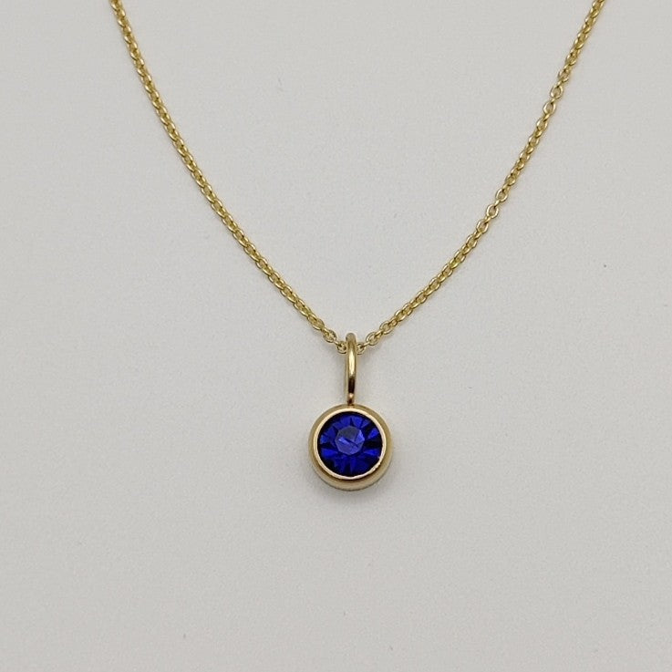 Gold necklace with a blue gemstone pendant on a light gray background