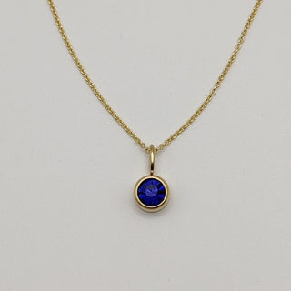 Gold necklace with a blue gemstone pendant on a light gray background