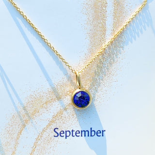 Gold necklace with a blue pendant on a light blue background
