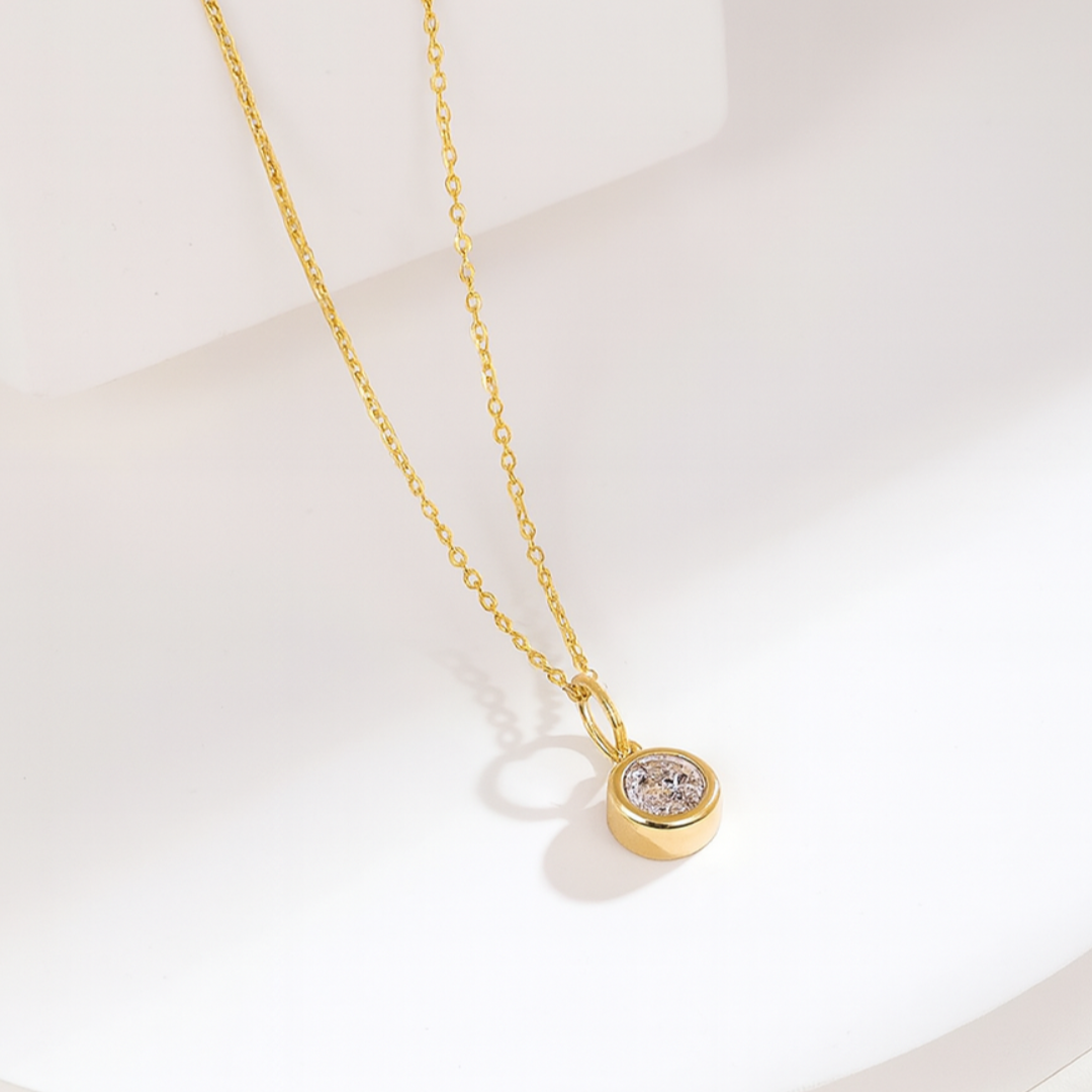 Gold necklace with a small round pendant on a light background