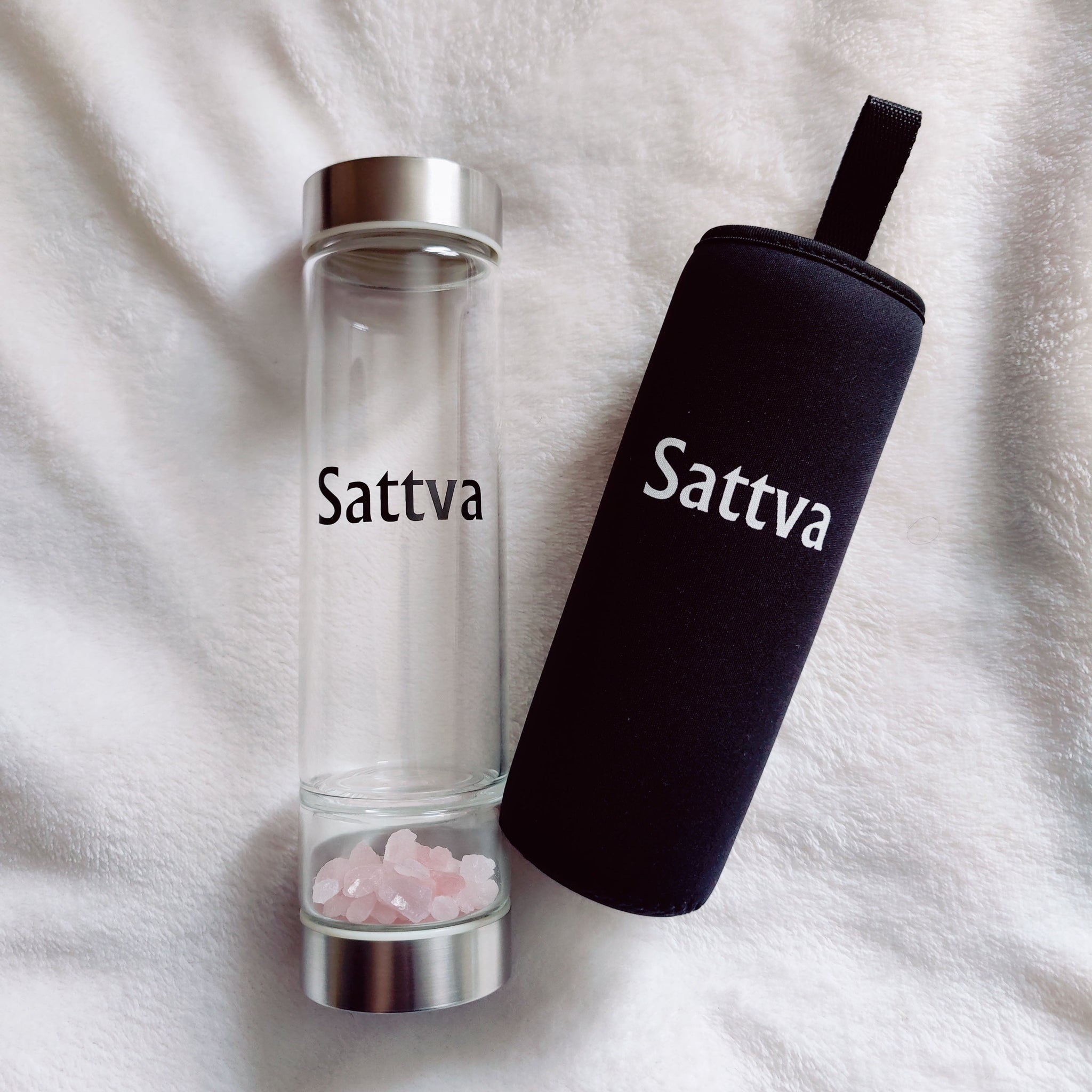 Clear glass bottle with silver cap and black sleeve labeled 'Sattva' on a white fabric background