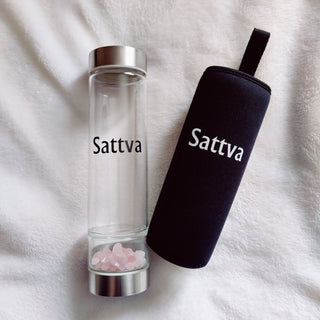 Clear glass bottle with silver cap and black sleeve labeled 'Sattva' on a white fabric background