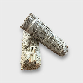 Two white sage smudge sticks tied with white string on a light gray background