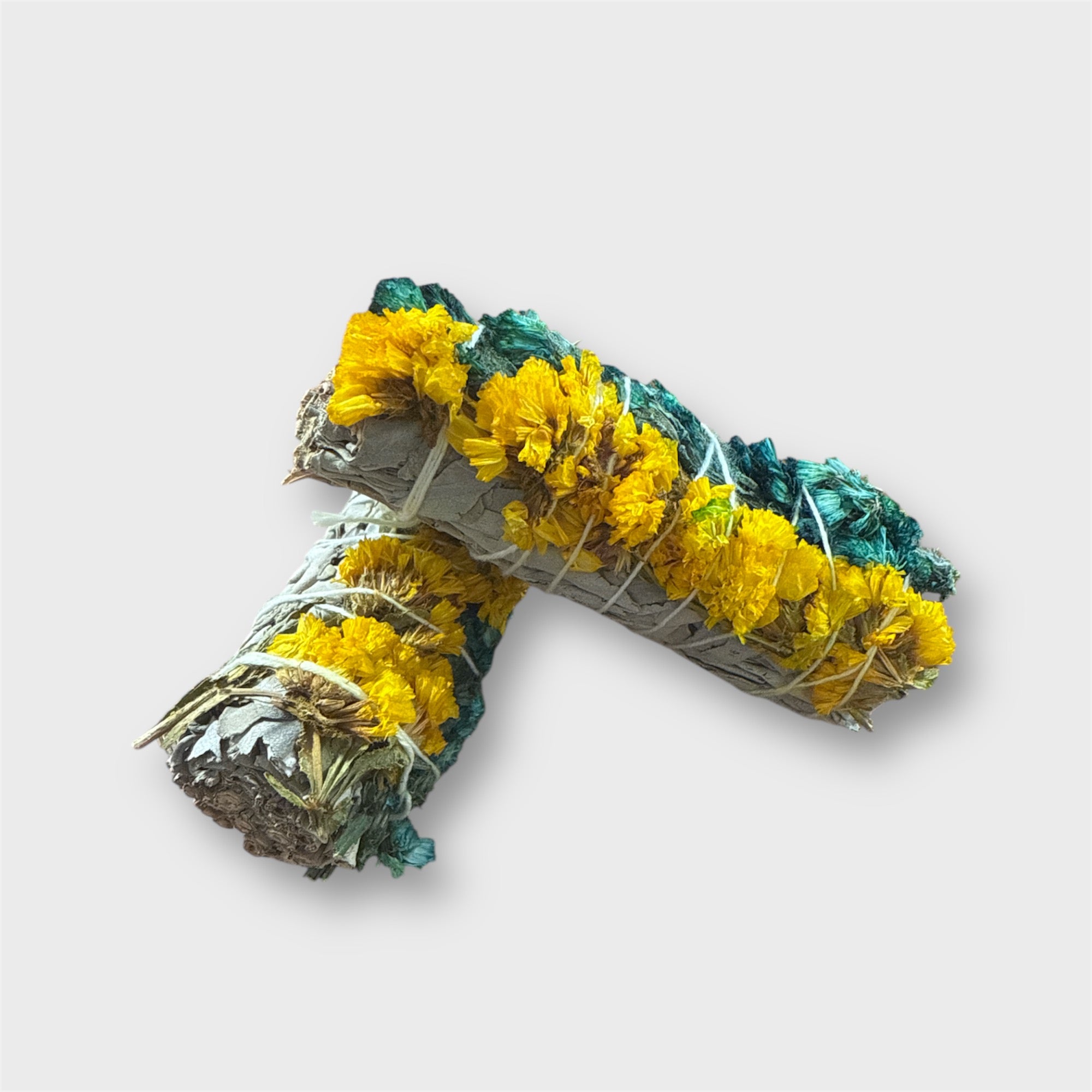 Two rolled white sage smudge stick bundle with yellow and green flowers on a light gray background