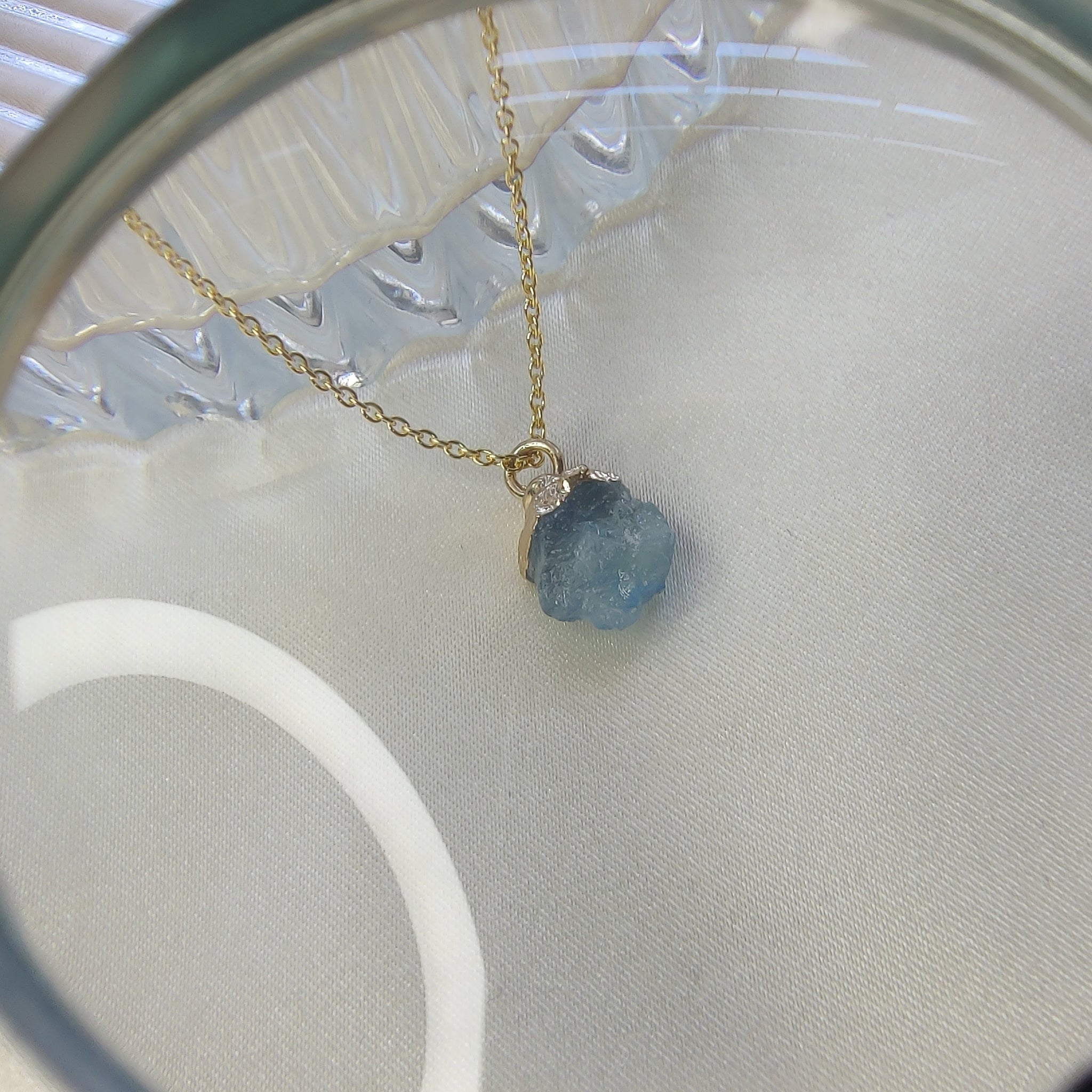 Necklace with a blue gemstone under a magnifying glass on a light background