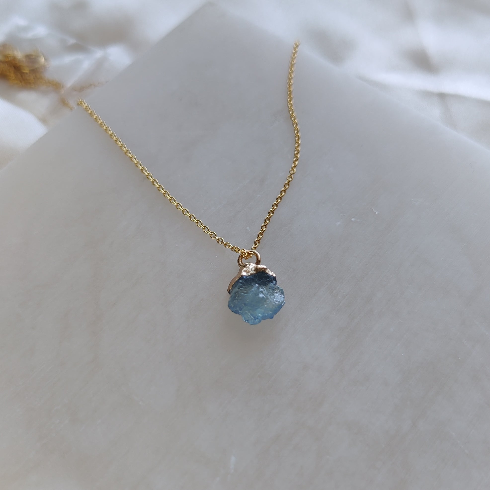 Gold necklace with a blue pendant on a white surface