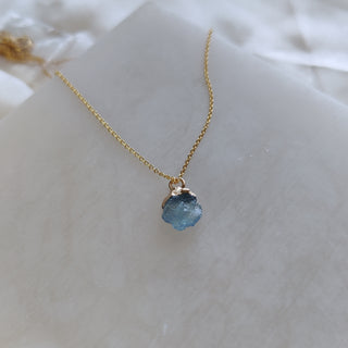 Gold necklace with a blue pendant on a white surface