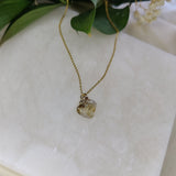 Gold necklace with a pendant on a white marble surface with green leaves and flowers.