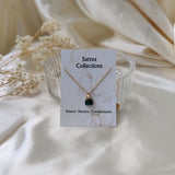 Gold necklace with a green pendant on a 'Sattva Collections' card against a soft beige background.