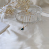 Necklace with a green pendant on a white surface with dried flowers and a glass dish.