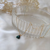 Gold necklace with a green pendant on a white surface with dried flowers.