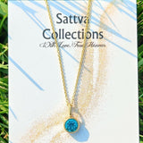Gold necklace with a blue gemstone on a 'Sattva Collections' card with grass in the background